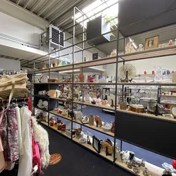 Verschillende tweedehands decoratieartikelen, servies en huishoudspullen uitgestald op metalen stellingen