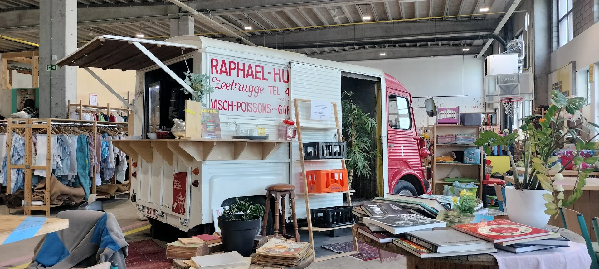 Winkelinterieur met vintage kampeerwagen, stellingen met spullen en groenplanten.