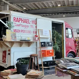 Winkelinterieur met vintage kampeerwagen, stellingen met spullen en groenplanten.
