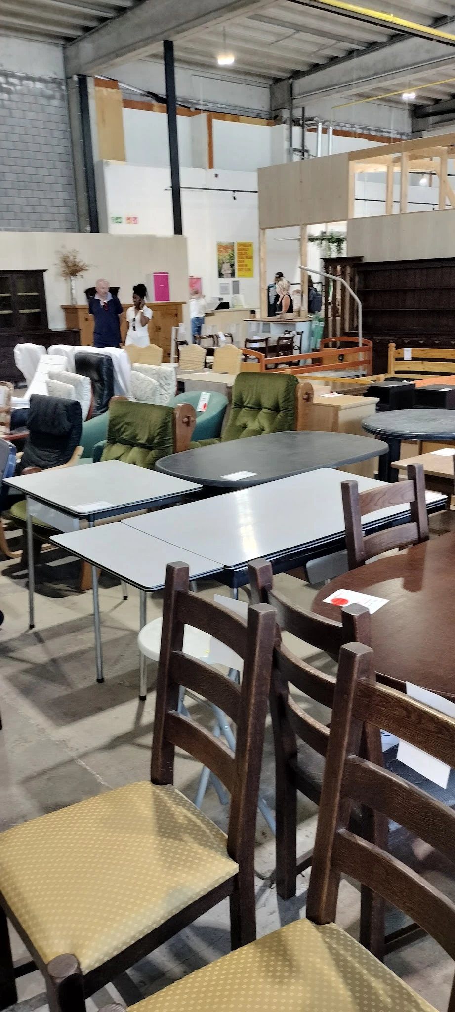 Uitgestalde meubels in een kringloopwinkel: tafels, stoelen en groene fauteuils