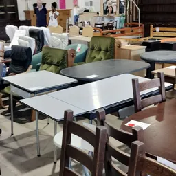 Uitgestalde meubels in een kringloopwinkel: tafels, stoelen en groene fauteuils