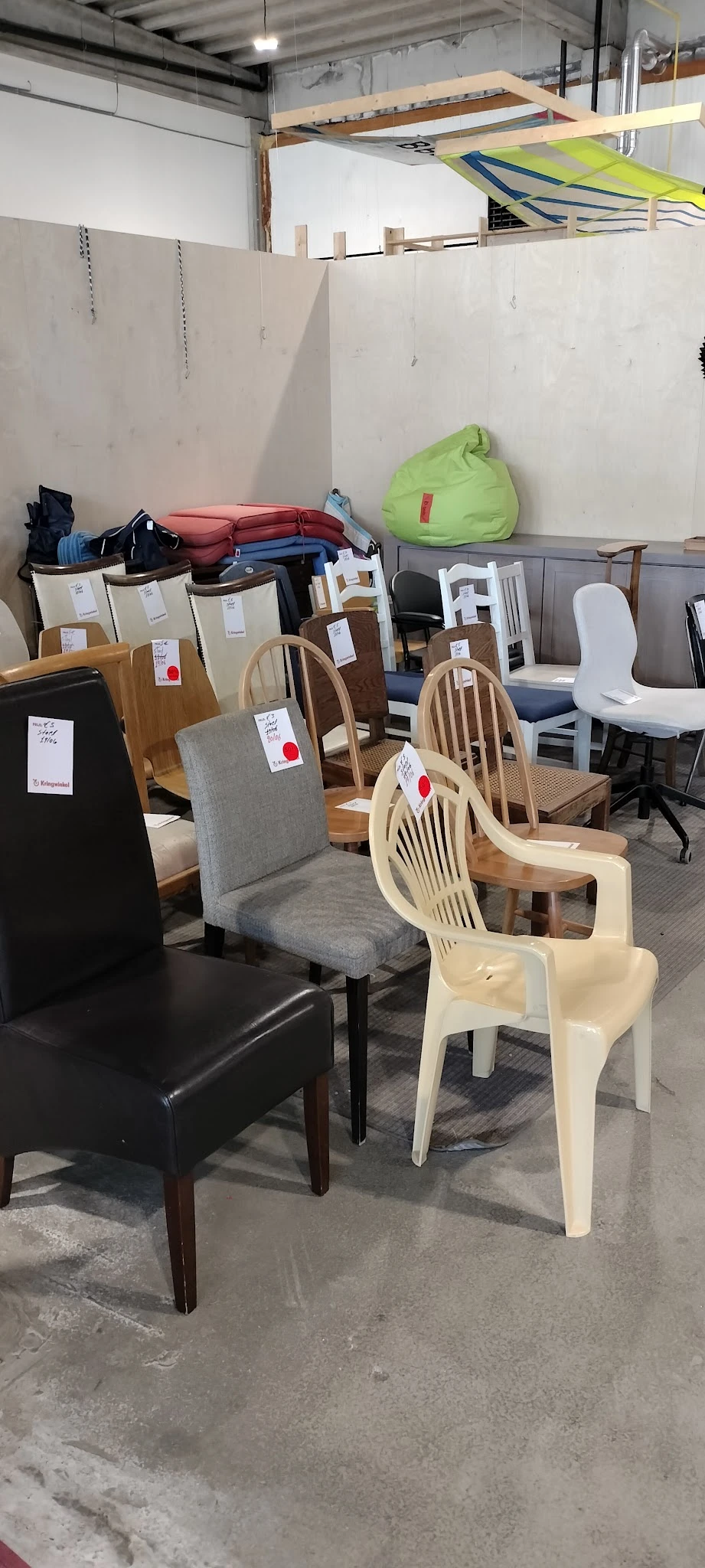 Verschillende houten en kunststof stoelen met prijskaartjes in een kringloopwinkel
