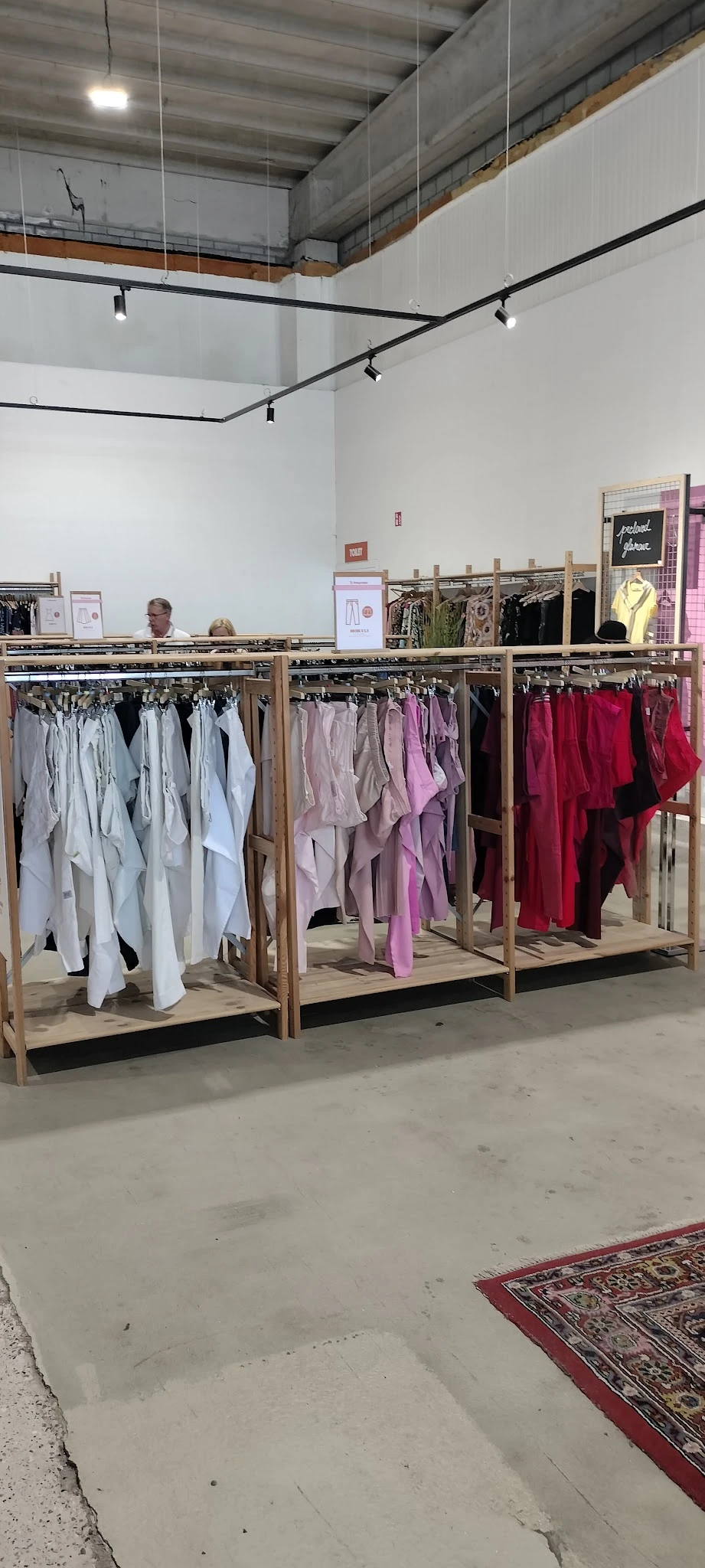 Drie houten rekken met uitgestalde dameskleding in verschillende kleuren: wit, roze/paars en rood