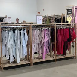Drie houten rekken met uitgestalde dameskleding in verschillende kleuren: wit, roze/paars en rood
