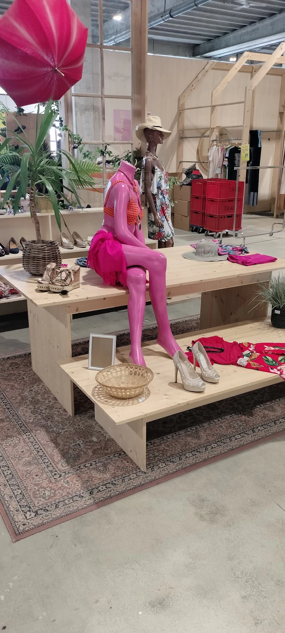 Uitstalling met roze mannequin, damessschoenen, kleding en decoratieve items op houten display