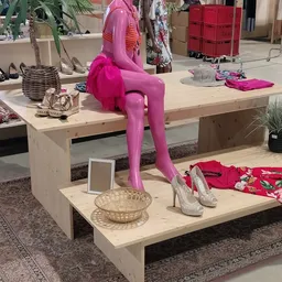 Uitstalling met roze mannequin, damessschoenen, kleding en decoratieve items op houten display