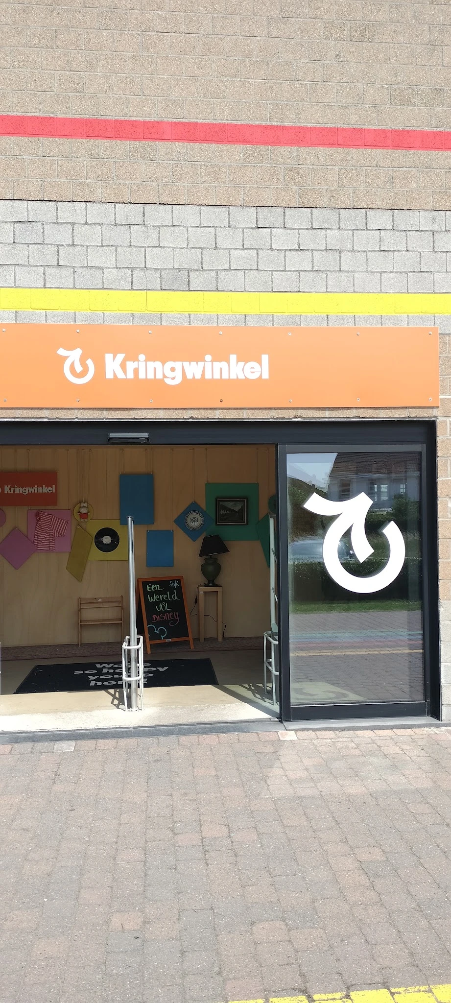 Gevel van kringloopwinkel met oranje uithangbord en uitgestalde spullen in etalage