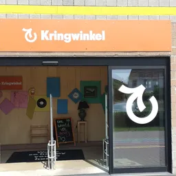 Gevel van kringloopwinkel met oranje uithangbord en uitgestalde spullen in etalage