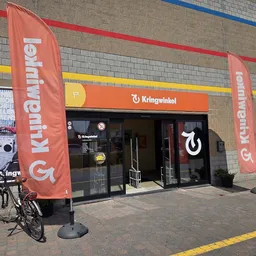 Winkelfront met rode banners en logo, fiets ervoor, bakstenen gevel met gekleurde strepen