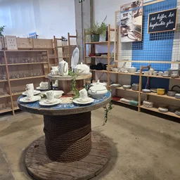 Winkelvloer met centrale tafel gemaakt van touw, uitgestalde serviesgoed, houten stellingen met huishoudartikelen en decorati