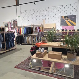 Winkelvloer met kledingrekken, houten display-tafels met plantenbakken en schoenenrek tegen de muur