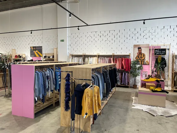 Ruime kringloopwinkel met kleding op rekken, roze displays en witte tegelwand