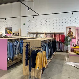 Ruime kringloopwinkel met kleding op rekken, roze displays en witte tegelwand