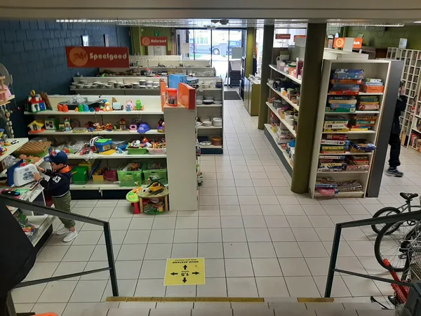 Winkelvloer met speelgoed en boekenrekken, gele waarschuwingsbord op de grond