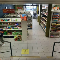 Winkelvloer met speelgoed en boekenrekken, gele waarschuwingsbord op de grond