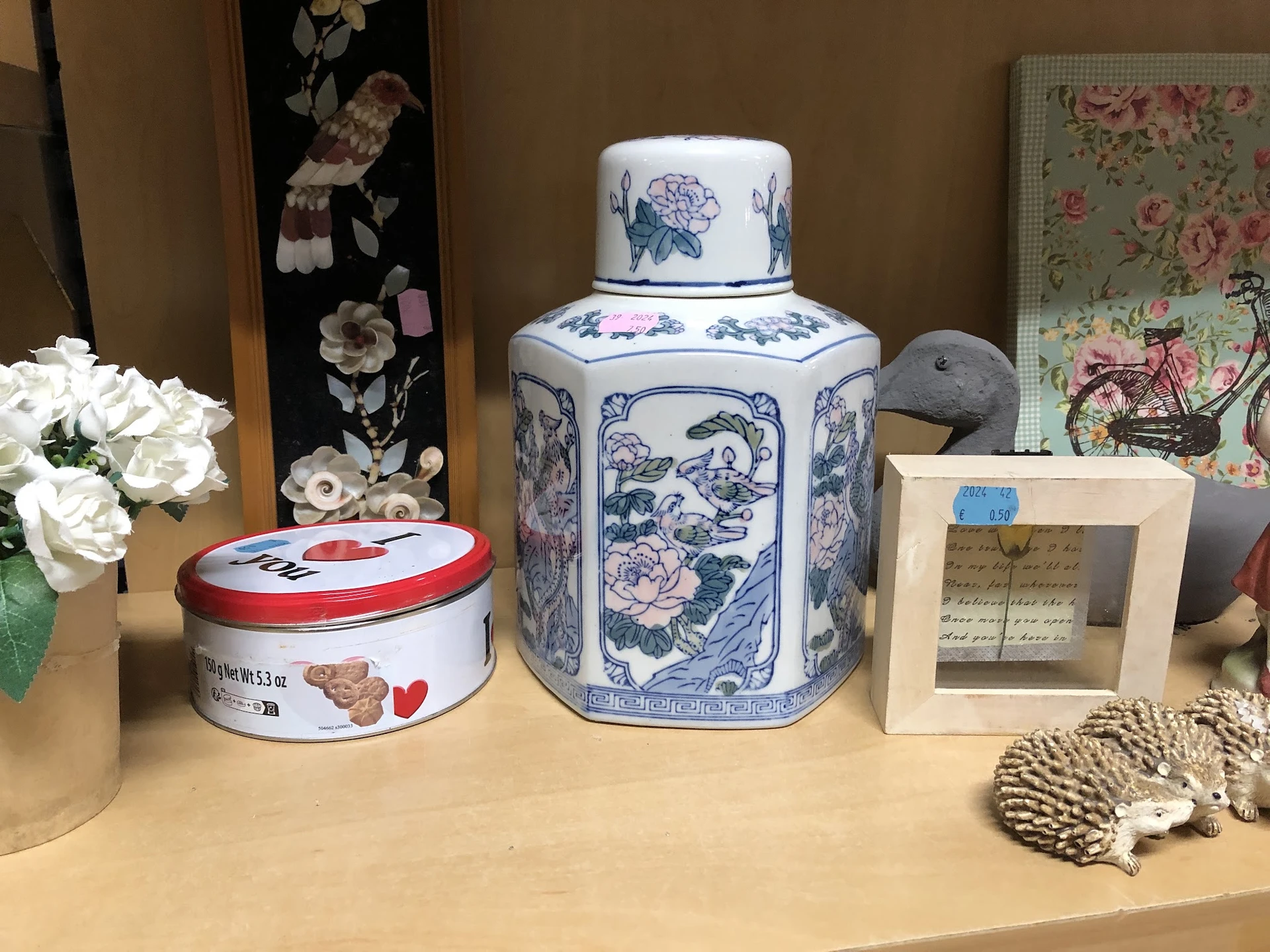 Uitgestalde decoratieve objecten: blauwe porseleinen thee-pot, rode blikje, witte kunstbloemen en overige huisraadadictelen o