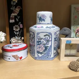 Uitgestalde decoratieve objecten: blauwe porseleinen thee-pot, rode blikje, witte kunstbloemen en overige huisraadadictelen o
