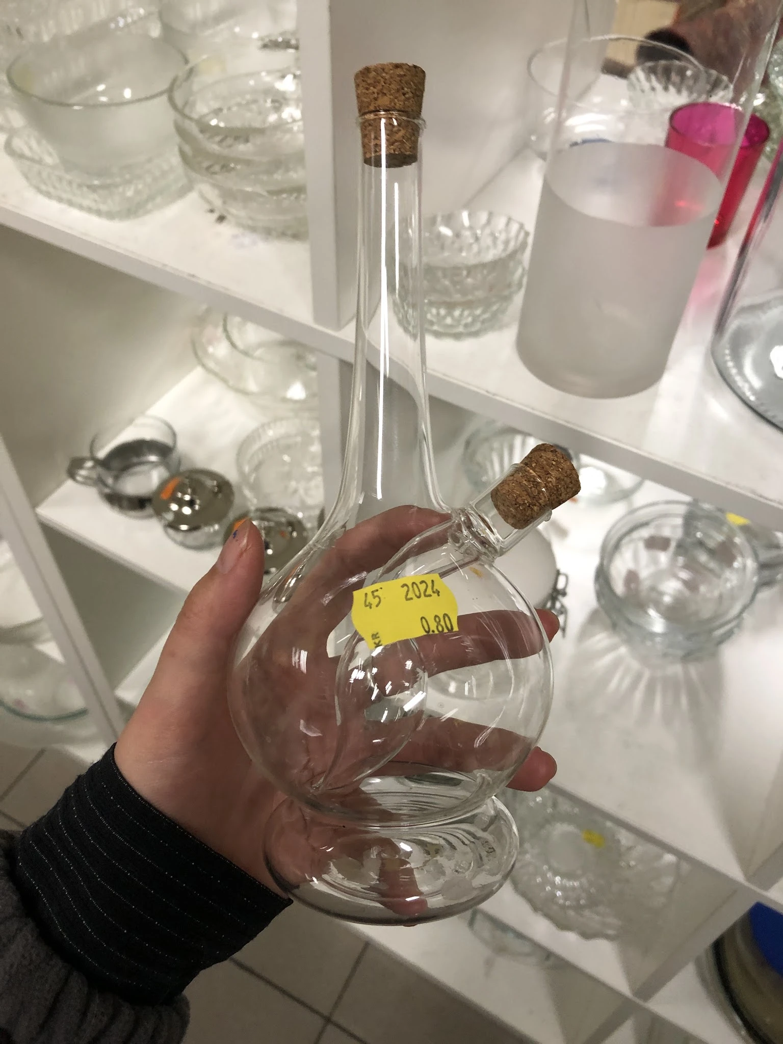 Glazen flesje met kurk en geel prijskaartje '45 2024 0.80' gehouden in hand