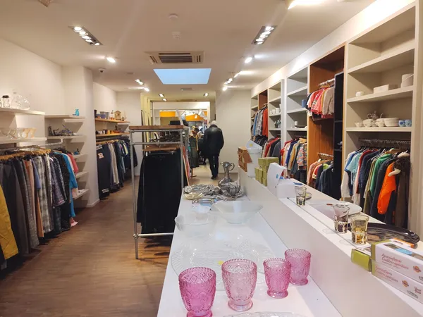 Ruim winkelinterieur met kledingrekken, witte stellingen met tweedehands kleding en accessoires, toonbank met roze glazen