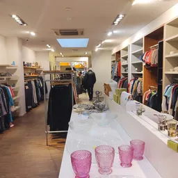 Ruim winkelinterieur met kledingrekken, witte stellingen met tweedehands kleding en accessoires, toonbank met roze glazen