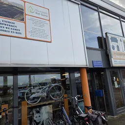 Voorgevel van kringloopwinkel met ramen, oranje accenten en fietsen in de etalage