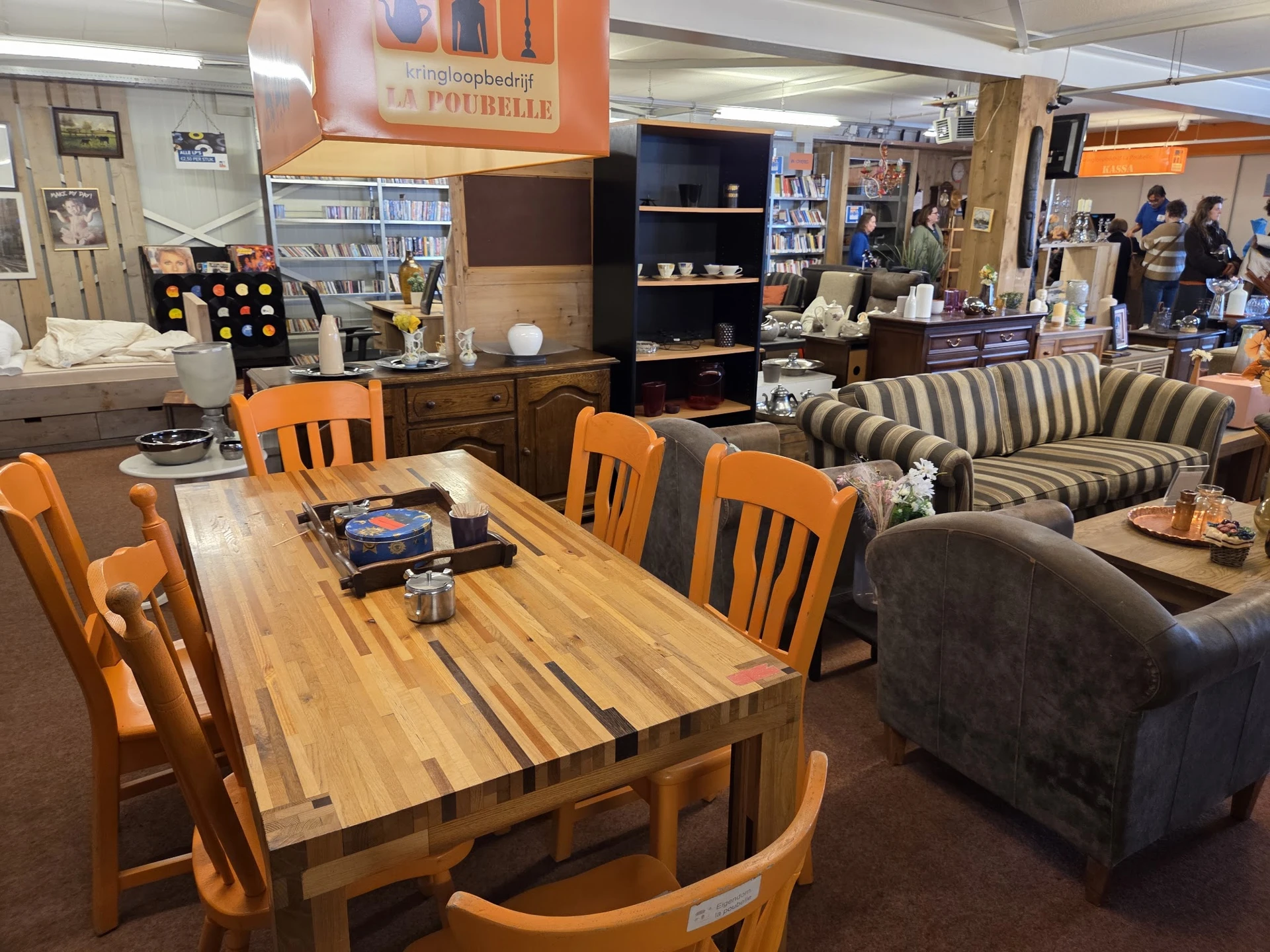 Winkelvloer met houten eettafel, oranje stoelen en gestreepte bank, boekenkasten en stellingen op de achtergrond