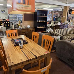 Winkelvloer met houten eettafel, oranje stoelen en gestreepte bank, boekenkasten en stellingen op de achtergrond