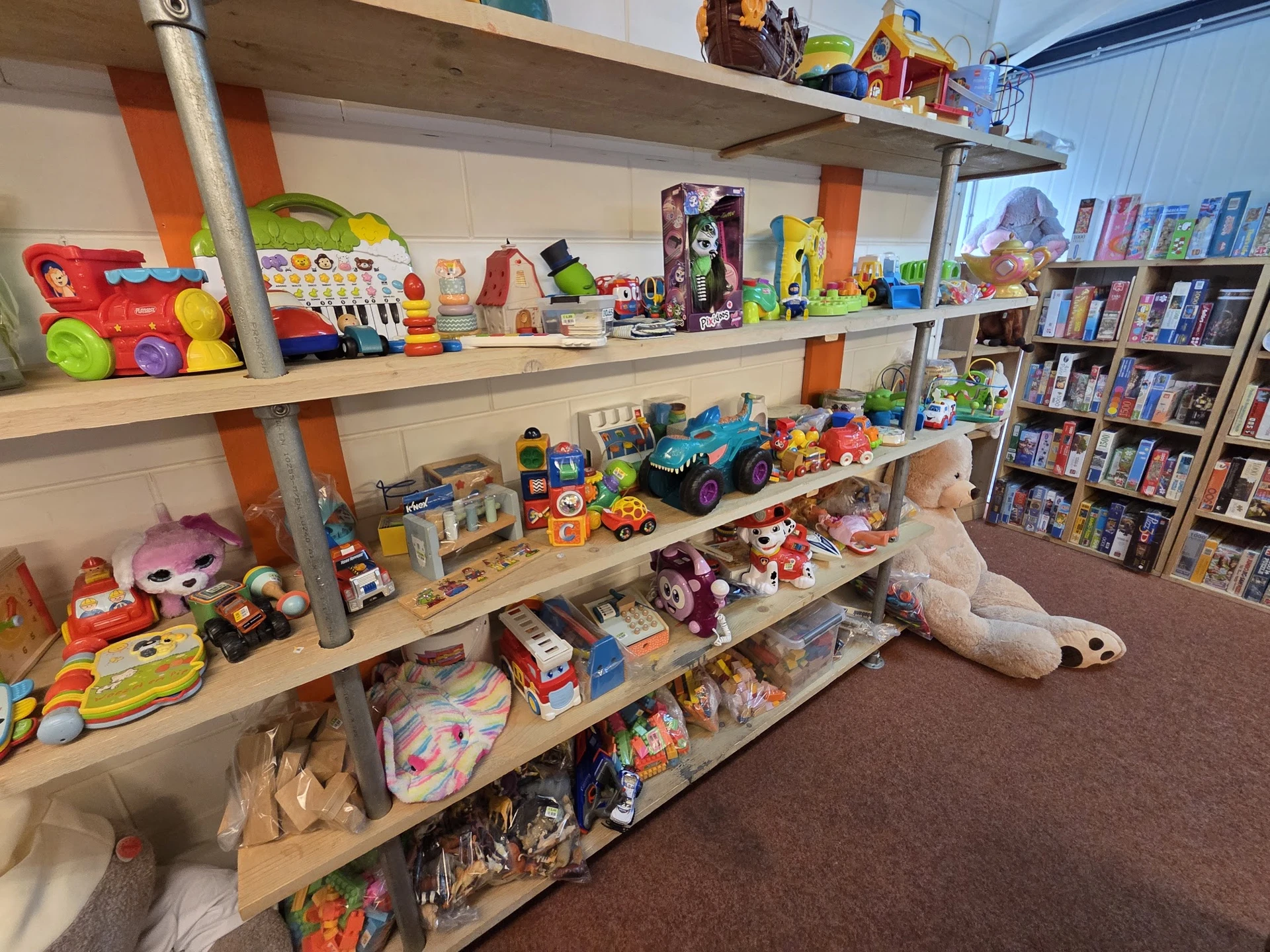 Houten stellingen vol met speelgoed, poppen, auto's en andere kinderartikelen in de kringloopwinkel