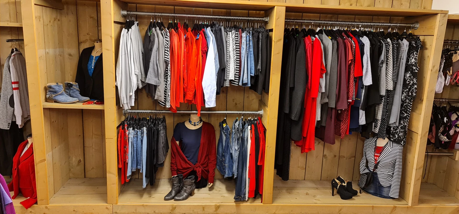 Houten stellingen met uitgestalde tweedehands kleding in verschillende kleuren, met rode, zwarte en grijze kledingstukken, sc