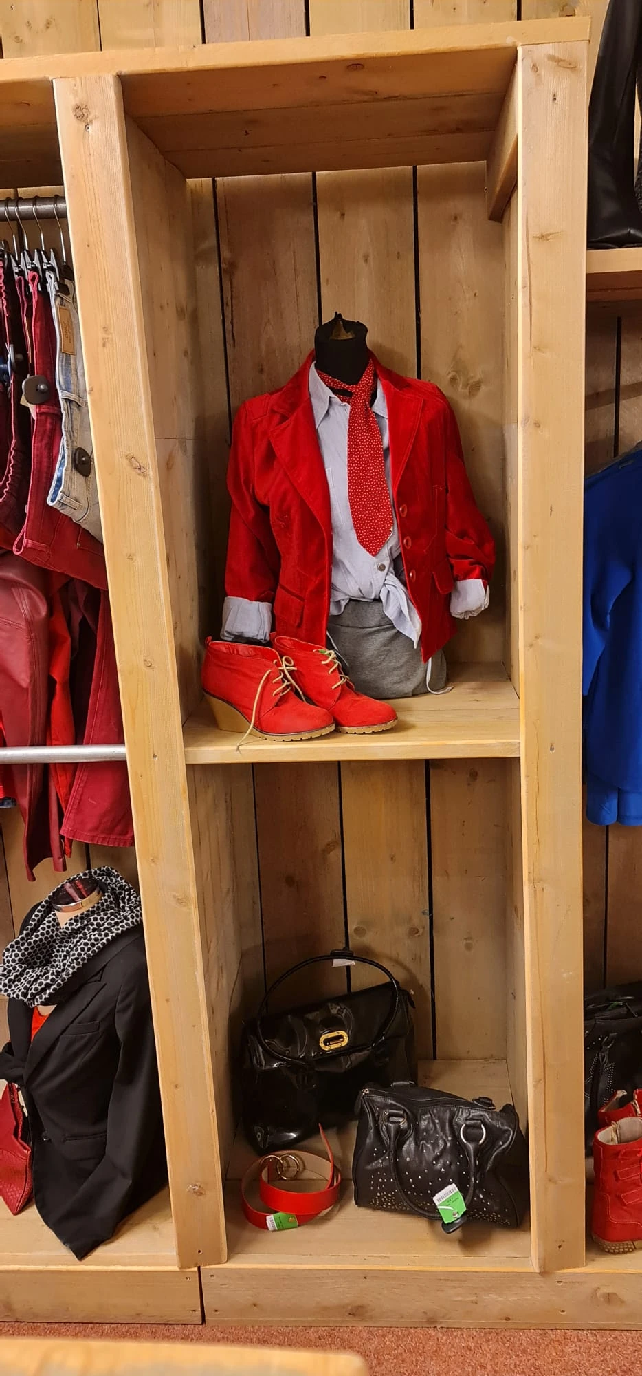 Houten kast met rode kinderkleding en rode schoenen in een kringloopwinkel