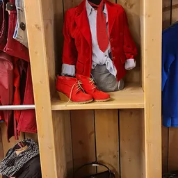 Houten kast met rode kinderkleding en rode schoenen in een kringloopwinkel