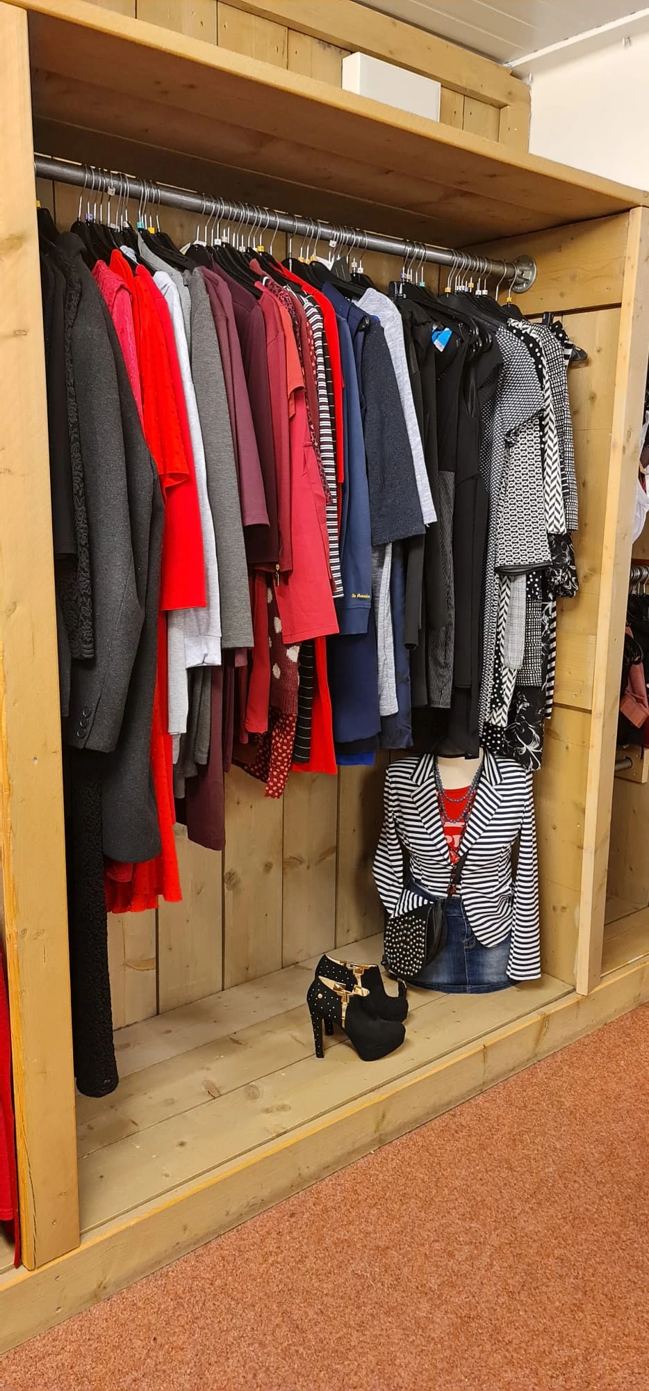Rekken met tweedehands kleding in verschillende kleuren en patronen, waaronder rode, zwarte, grijze en gestreepte kledingstuk