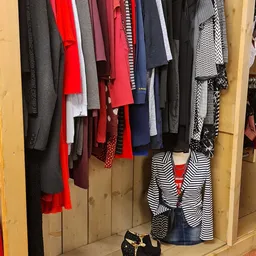 Rekken met tweedehands kleding in verschillende kleuren en patronen, waaronder rode, zwarte, grijze en gestreepte kledingstuk