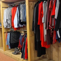 Houten stellingkast met tweedehands kleding in verschillende kleuren, waaronder rode, zwarte en grijze kledingstukken op hang