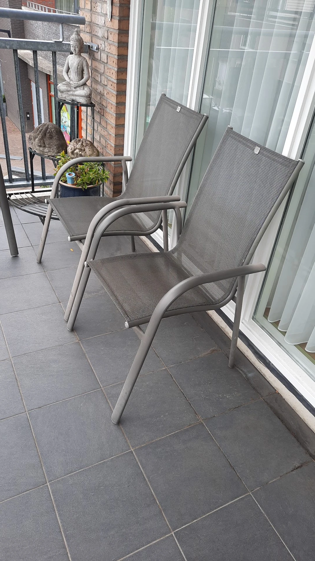 Grijze tuinstoelen op een terras naast een gebouw