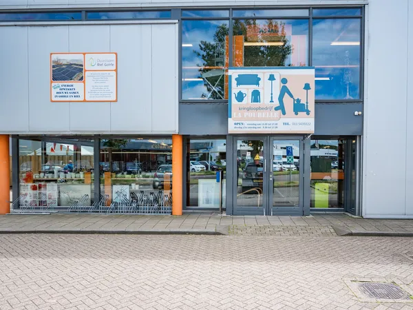 Gevel van kringloopwinkel met orange en blauwe accenten, etalages met spullen en informatieborden