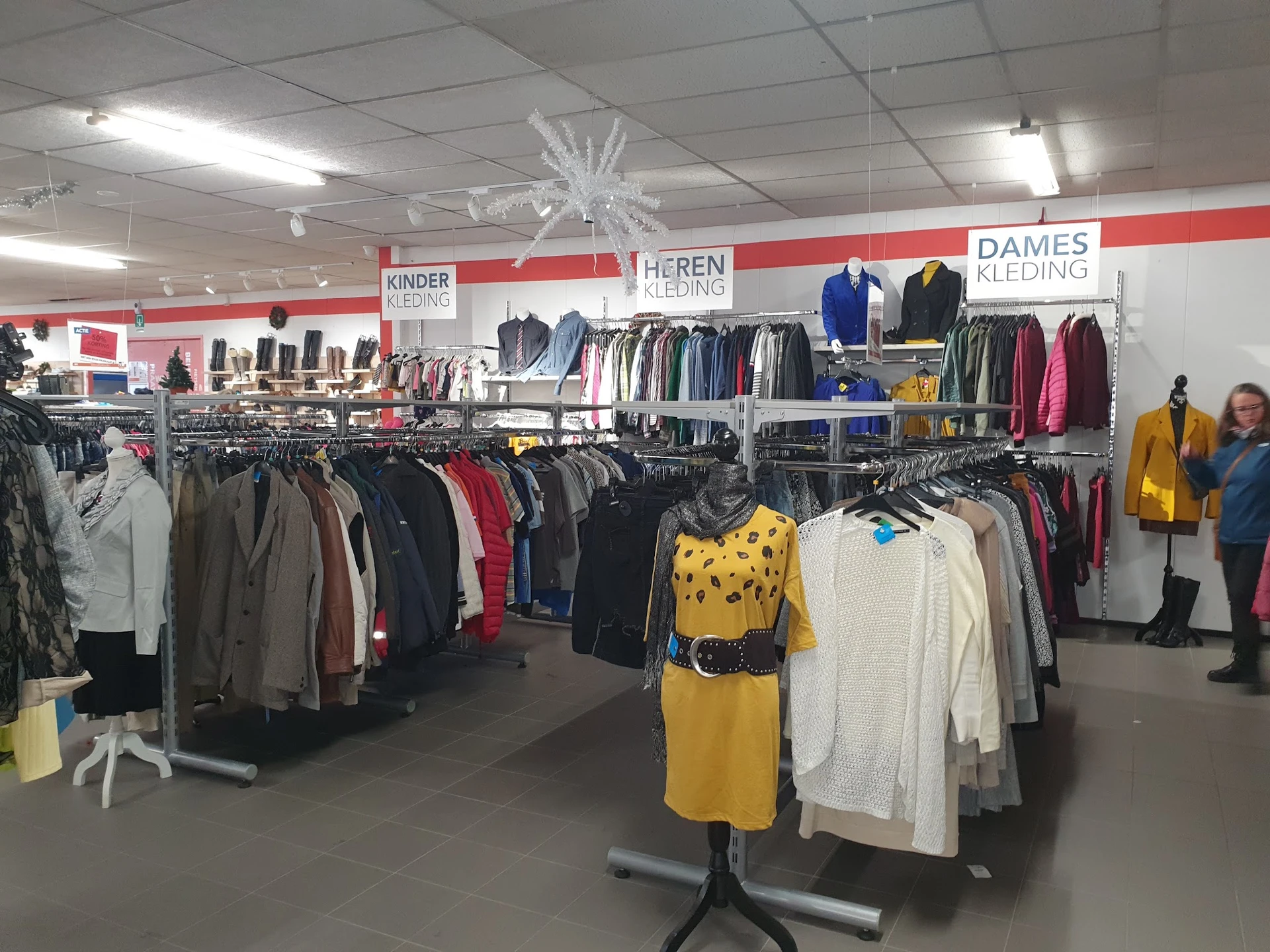Overzicht van de winkelvloer met rekken tweedehands kleding, onderverdeeld in secties voor kinderen, heren en dames