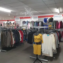 Overzicht van de winkelvloer met rekken tweedehands kleding, onderverdeeld in secties voor kinderen, heren en dames