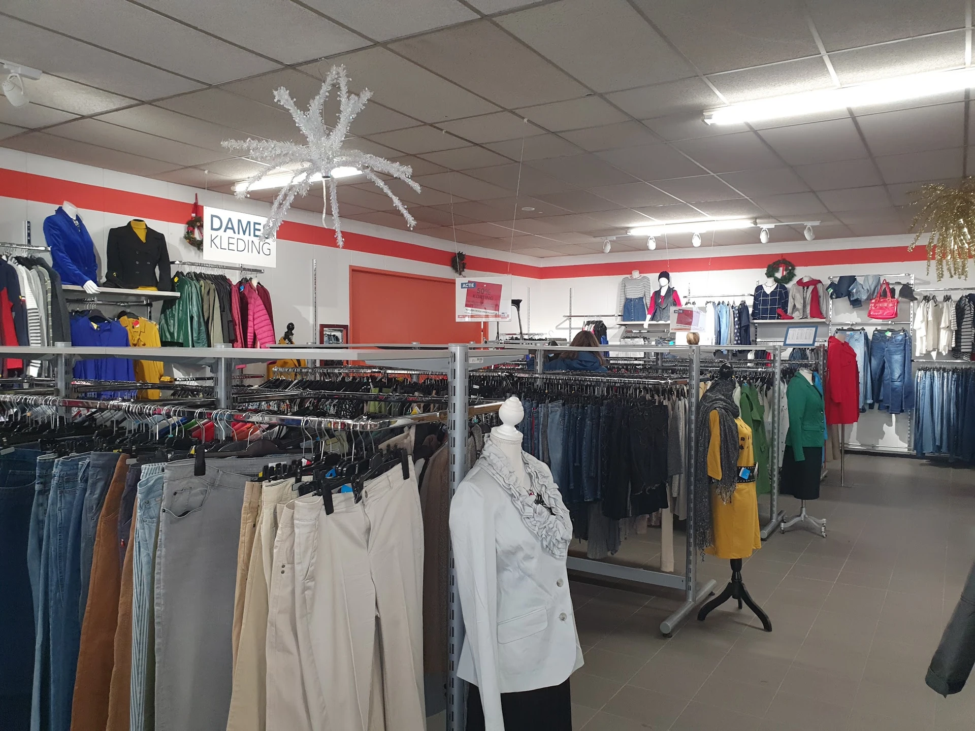 Winkelvloer met kledingrekken vol tweedehands kleding, rode wandstrepen en decoratieve witte ster aan plafond