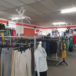Winkelvloer met kledingrekken vol tweedehands kleding, rode wandstrepen en decoratieve witte ster aan plafond