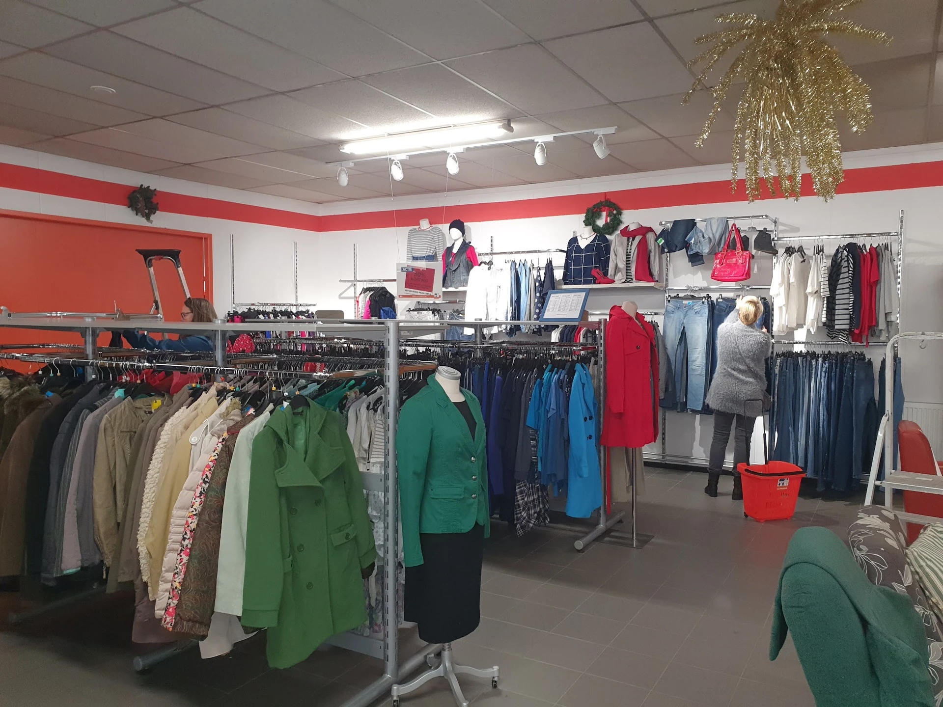 Winkelvloer met rekken vol tweedehands kleding in verschillende kleuren, gouden decoratie boven en rode accenten in het inter