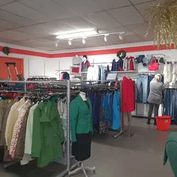 Winkelvloer met rekken vol tweedehands kleding in verschillende kleuren, gouden decoratie boven en rode accenten in het inter