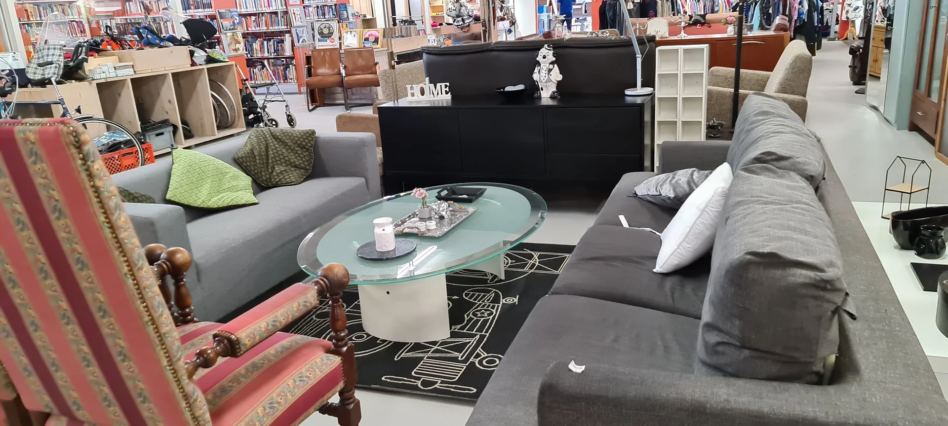Woonkamerinrichting met grijze banken, glazen salontafel, zwart dressoir en boekenkast in een kringloopwinkel