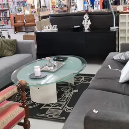 Woonkamerinrichting met grijze banken, glazen salontafel, zwart dressoir en boekenkast in een kringloopwinkel