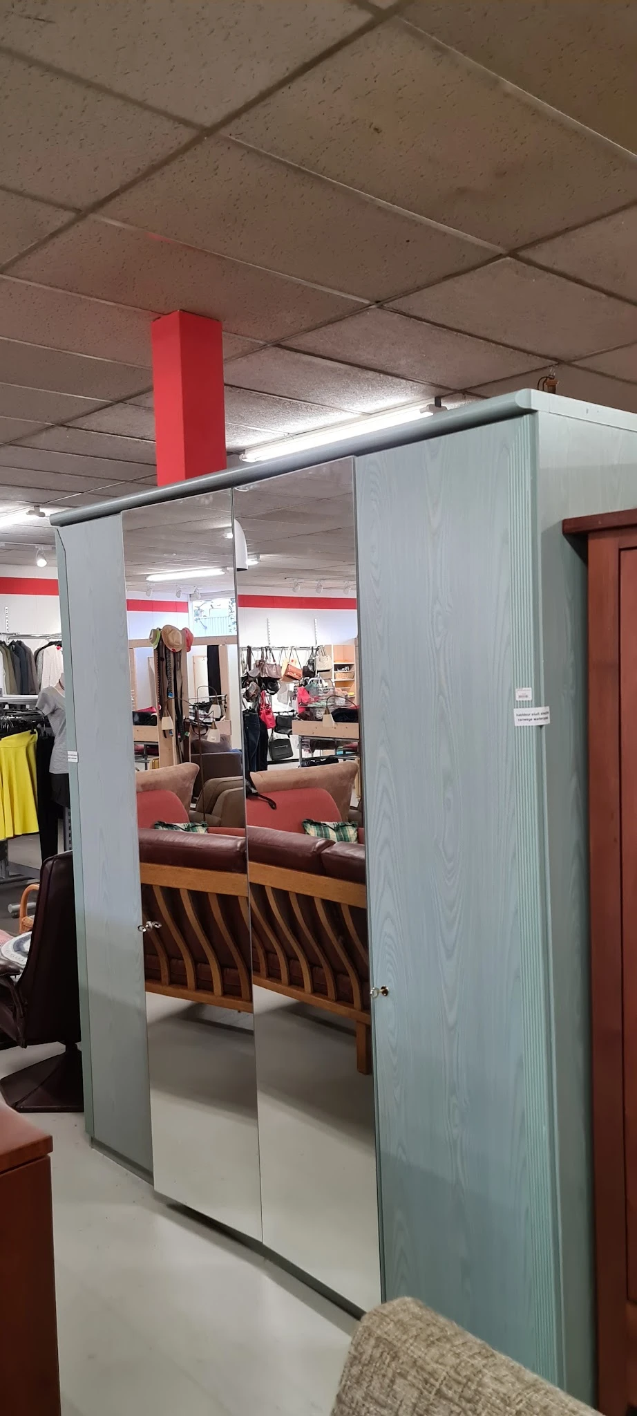 Spiegelwand in kledingafdeling met zicht op winkelrekken met tweedehands kleding