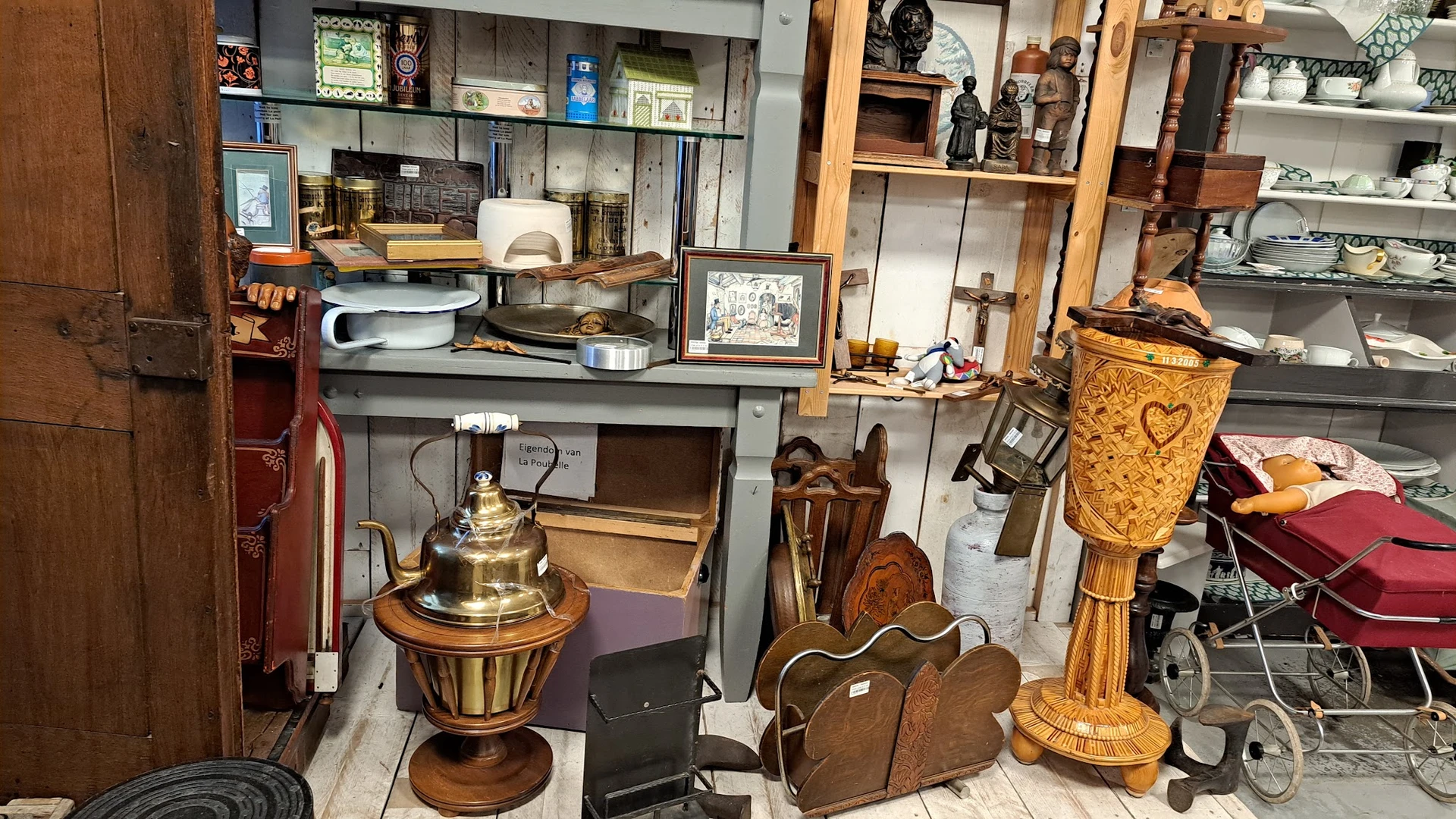 Diverse tweedehandsartikelen zoals houten meubels, koperen decoratiestukken, manden en serviesgoed op uitstalling in de winke