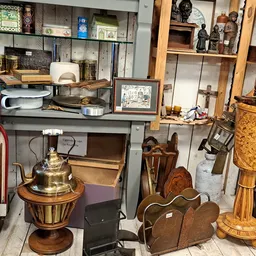 Diverse tweedehandsartikelen zoals houten meubels, koperen decoratiestukken, manden en serviesgoed op uitstalling in de winke