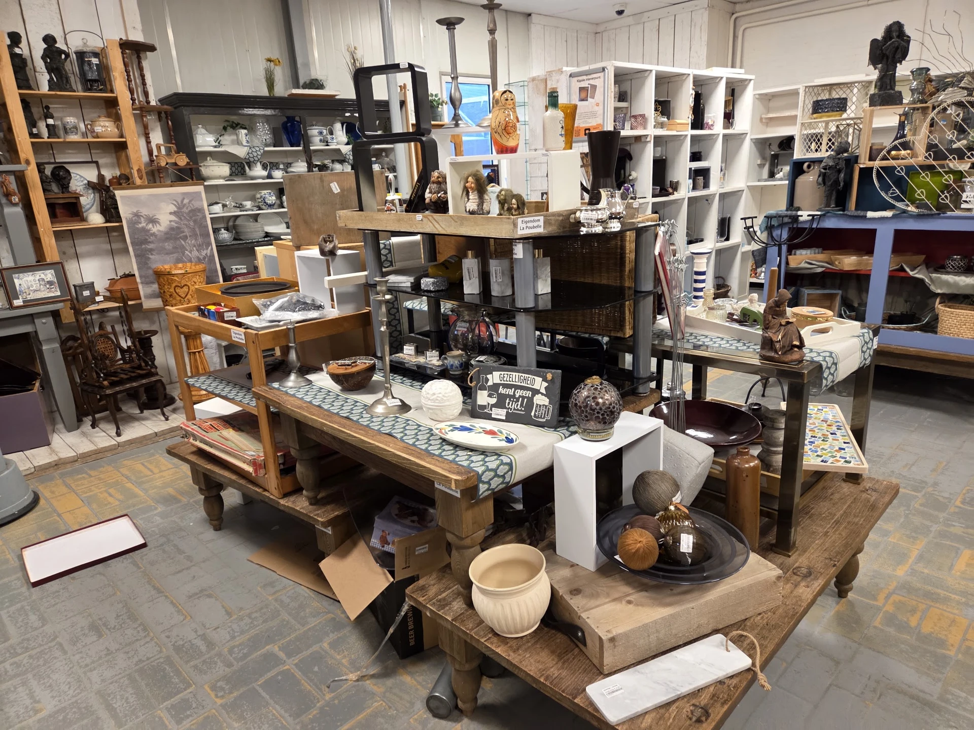 Winkelvloer met houten tafels en stellingen vol huishoudelijke spullen, servies en decoratieartikelen