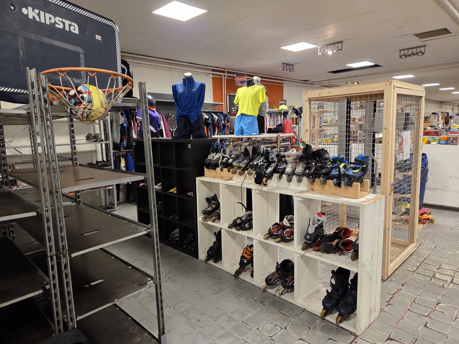 Uitgestalde sportschoenen en -kleding in kasten en op display, met basketbalring op achtergrond