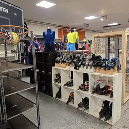Uitgestalde sportschoenen en -kleding in kasten en op display, met basketbalring op achtergrond